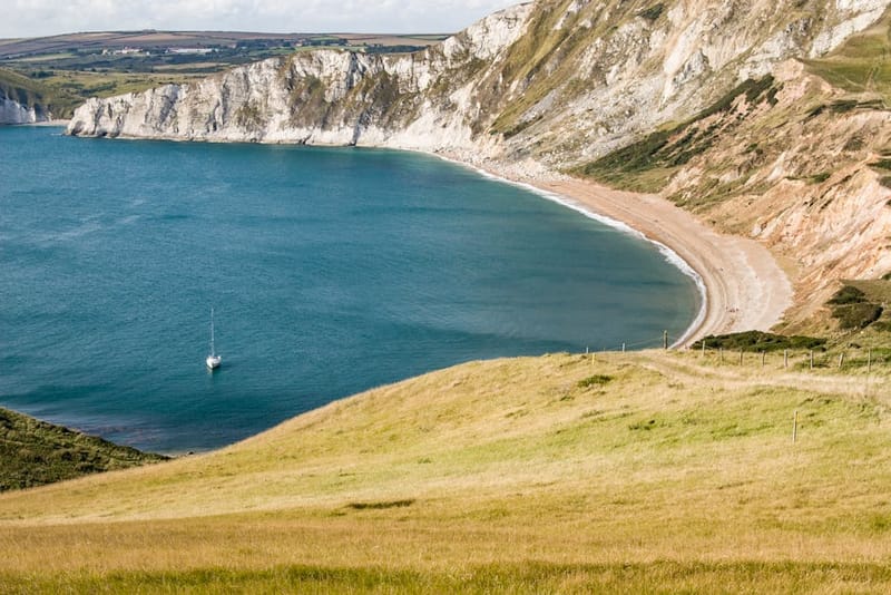 Beautiful view of a coastline with cliffs, a sandy beach, and a lone sailboat at sea.