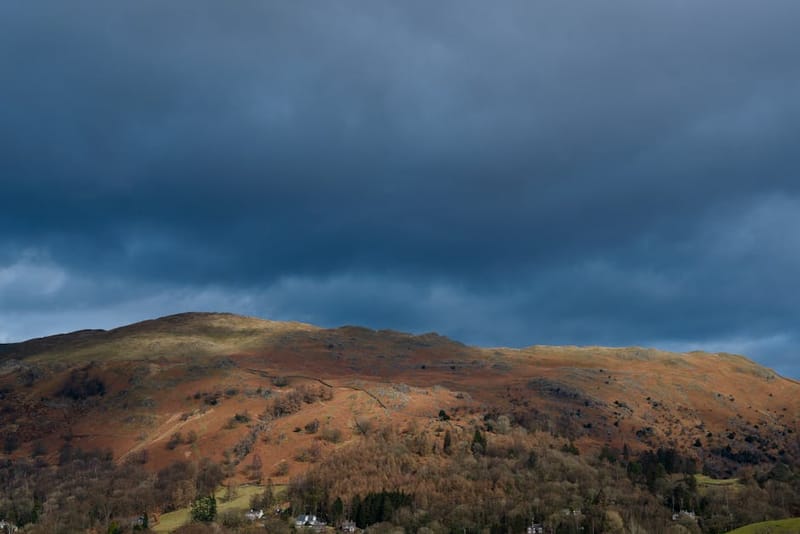 Breathtaking view of Grasmere's autumn landscape with dramatic dark clouds and vibrant fall colors.