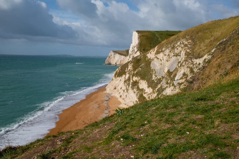 Dramatic view of the iconic cliffs along England's Jurassic Coast with turquoise sea and sandy beach.
