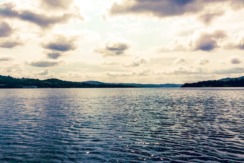 Peaceful Lake Windermere scene with calm waters and dramatic clouds in the scenic Lake District, England.