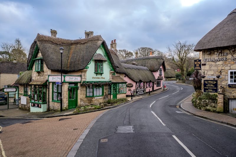 Picturesque street in an English village with traditional thatched roof buildings and shops.