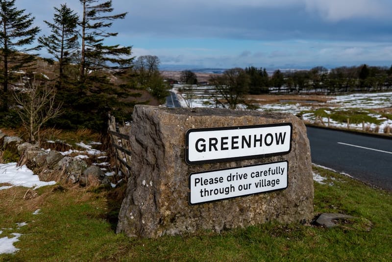 View of Greenhow village sign with a snowy countryside background, capturing winter serenity and rural charm.